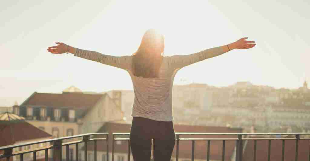Mujer joven, frente al balcón de un pueblo europeo, disfrutando el sol y la vida.